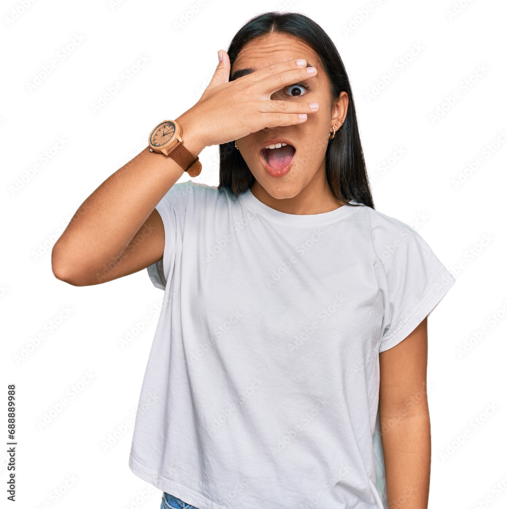 Φωτογραφία Young asian woman wearing casual white t shirt peeking in shock covering face and eyes with hand, looking through fingers with embarrassed expression