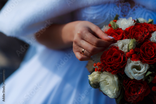 Hands of a newly-married couple with wedding rings on a wedding bouquet of the bride. Bouquet of red and pink roses. Wedding jewelery.