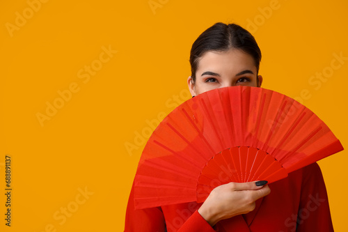 Beautiful young woman with fan on yellow background. Chinese New Year celebration