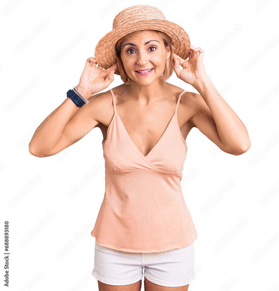 Young blonde woman wearing summer hat smiling pulling ears with fingers, funny gesture. audition problem Young blonde woman wearing summer hat smiling pulling ears with fingers, funny gesture. audition problem