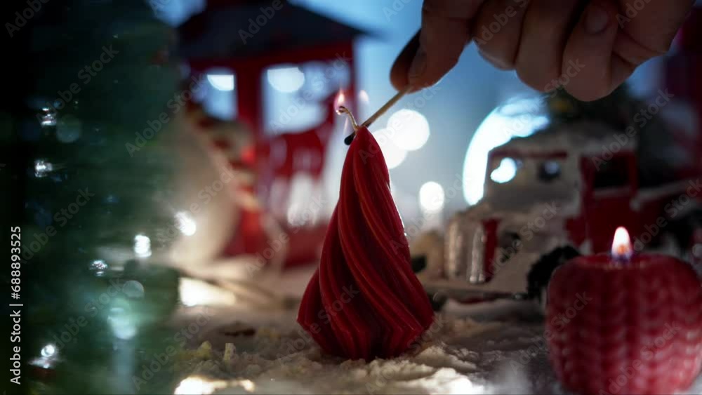 A static shot in which a close-up hand lights a Christmas candle in the shape of a fir tree. An atmospheric space with miniature snow-covered figures. A static shot in which a close-up hand lights a Christmas candle in the shape of a fir tree. An atmospheric space with miniature snow-covered figures.