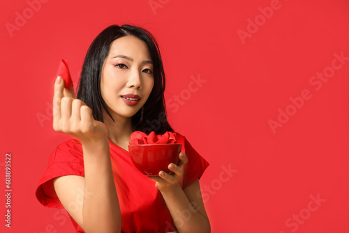 Beautiful young Asian woman with bowl of fortune cookies on red background. Chinese New Year celebration