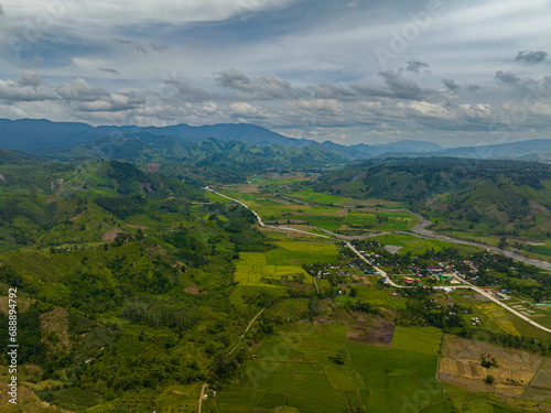 Fototapeta Naklejka Na Ścianę i Meble -  Green hills with paddy farmlands and water flowing over rivers. Blue sky and clouds. Mindanao, Philippines.