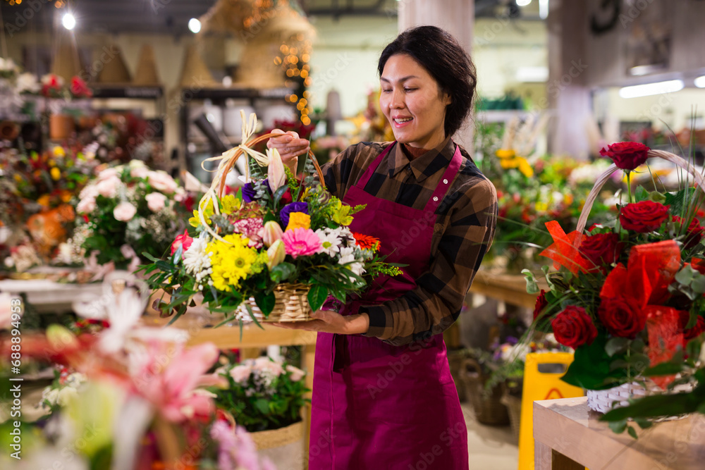 Middle age asian female florist in apron holding composition from natural flowers at flower shop