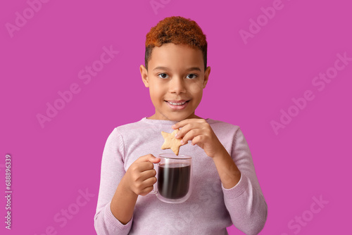 Cute little African-American boy with cookie and glass cup of hot chocolate on purple background