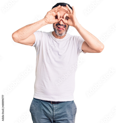 Middle age handsome man wearing casual t-shirt doing ok gesture like binoculars sticking tongue out, eyes looking through fingers. crazy expression.