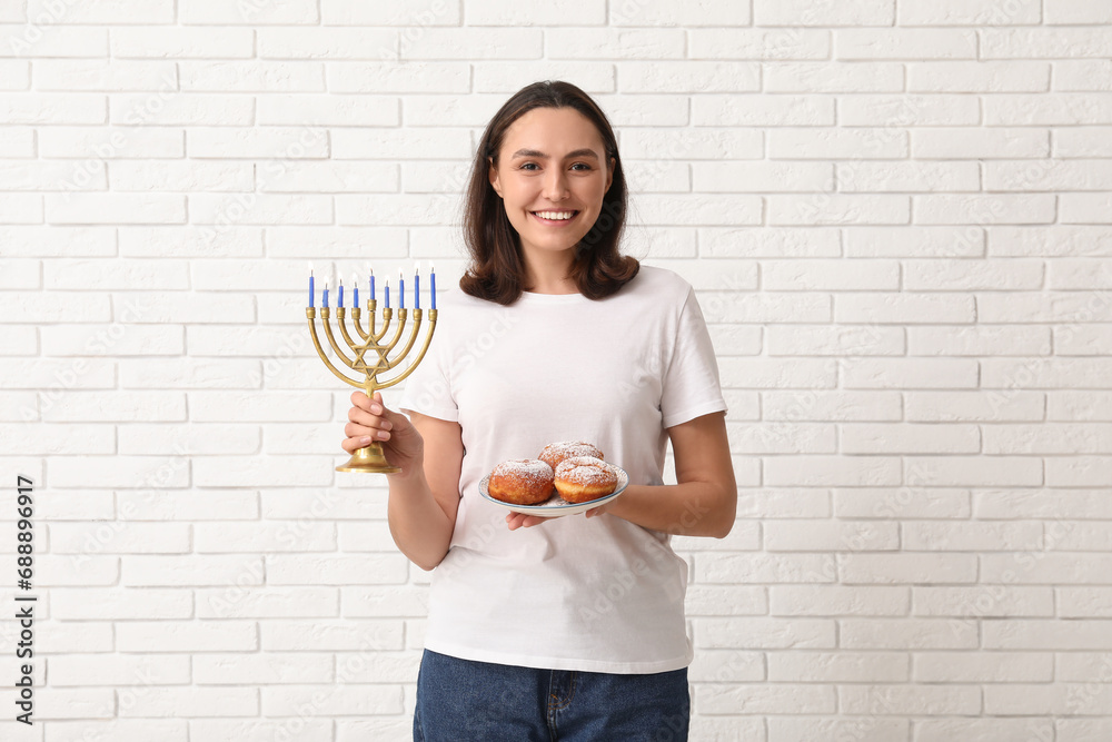 Pretty young woman with sufganiyots and menorah on white brick wall background. Hanukkah celebration Pretty young woman with sufganiyots and menorah on white brick wall background. Hanukkah celebration