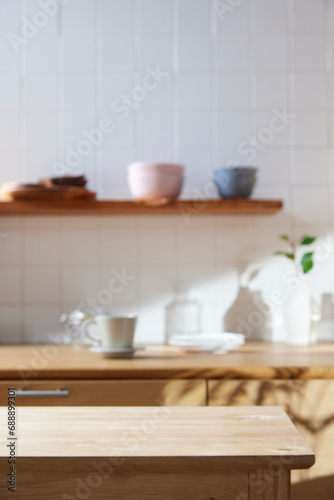 A sunny kitchen with white tile walls, a wooden table and sink.