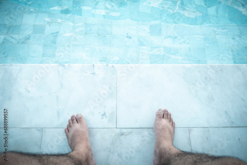 Relaxing man with his feet on poolside at swimming pool. Close up photo