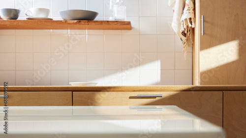 A sunny kitchen with white tile walls, a wooden table and sink.
