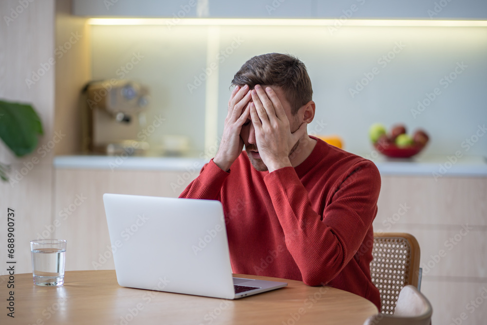 Worried man has financial difficulties after fired job closing face by hands sitting with laptop on kitchen at home. Unhappy depressed guy feeling apathy, desperation has bankruptcy, working failure Worried man has financial difficulties after fired job closing face by hands sitting with laptop on kitchen at home. Unhappy depressed guy feeling apathy, desperation has bankruptcy, working failure