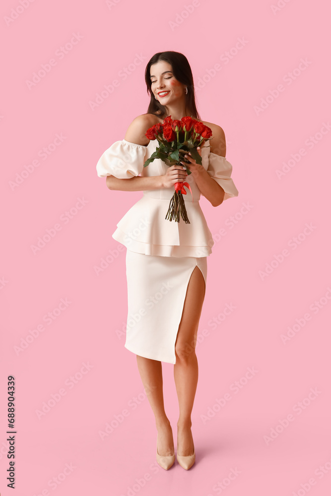 Happy young woman with kiss marks on her face and bouquet of roses on pink background