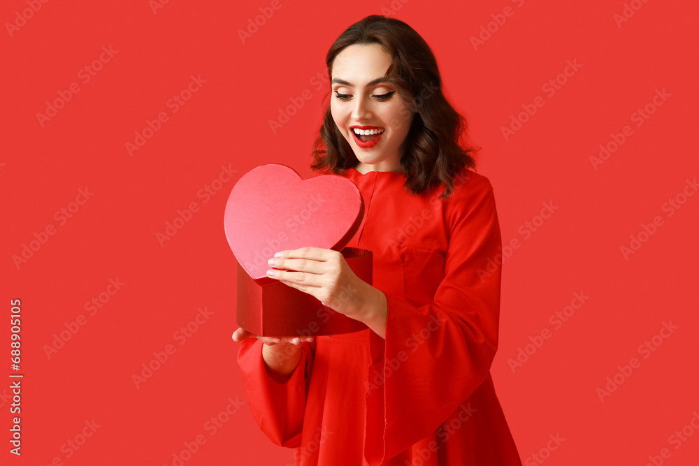 Surprised young woman with heart shaped gift box on red background Surprised young woman with heart shaped gift box on red background