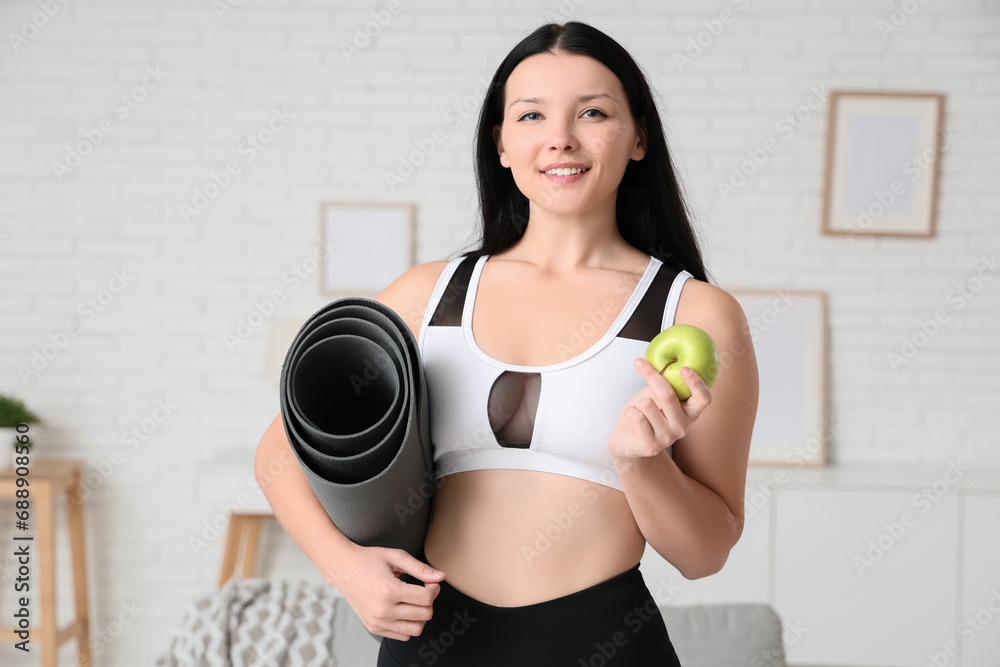 Beautiful young sporty woman with fresh apple and yoga mat at home. Weight loss concept Beautiful young sporty woman with fresh apple and yoga mat at home. Weight loss concept