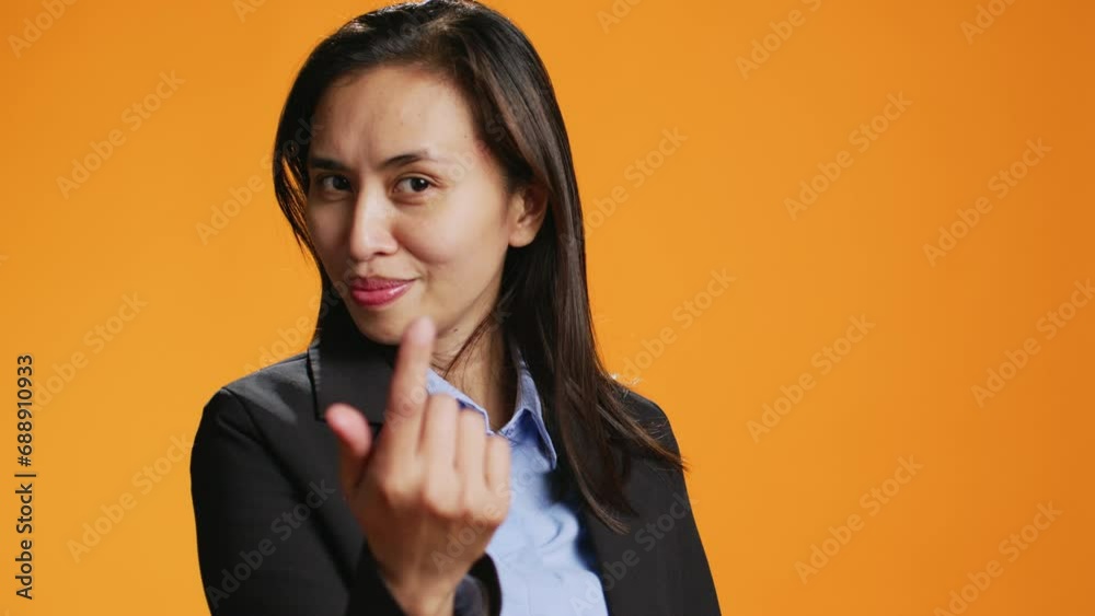 Female model calling for someone on camera, doing hailing gesture against orange background. Asian woman with office clothing inviting person to come closer, friendly adult. Female model calling for someone on camera, doing hailing gesture against orange background. Asian woman with office clothing inviting person to come closer, friendly adult.