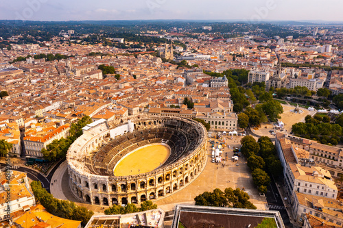 Drone view of ancient Roman amphitheatre Arena of Nimes on background of reddish tiled roofs of residential buildings on summer day, France photo