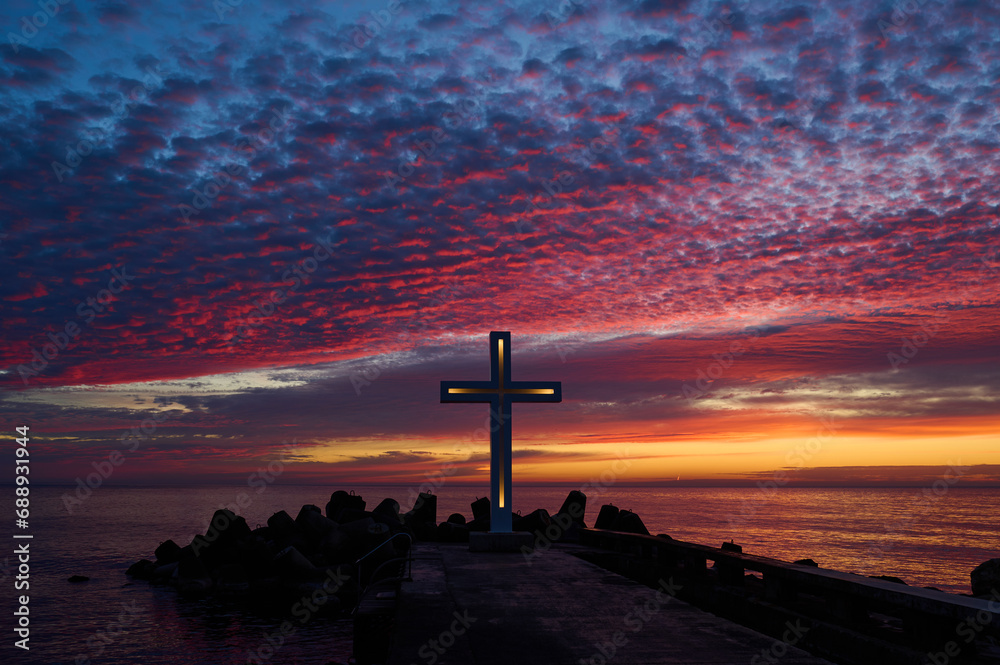 Christian Holy cross early in the morning at sunrise. The large cross stands on the edge of a breakwater on the sea coast - obrazy, fototapety, plakaty 