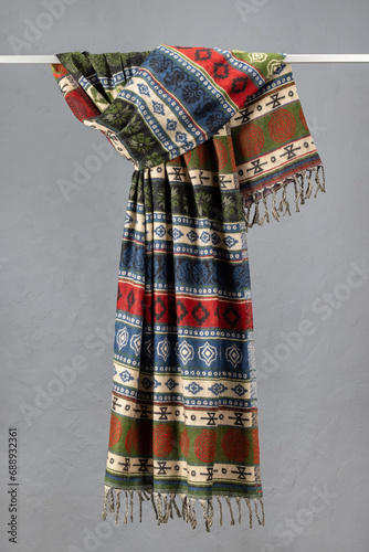 Cashmere scarf with fringe hanging on a hanger. Home comfort. Colorful plaids on a gray background.