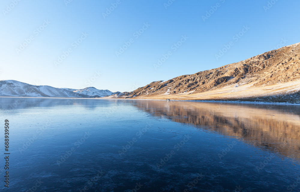 Winter landscape of frozen Baikal Lake in January at sunset. Tourists come to shore of iced bay to walk on clean thin ice and go ice skating. Winter active ice travel. Empty space for text