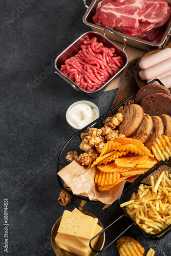 Saturated and trans. Unhealthy food. Sausage, potato, meat, cheese, popcorn, cookies, cream on dark background