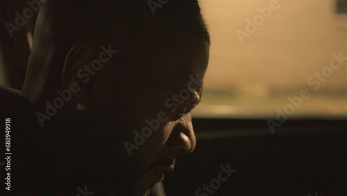 a black man sitting in the drivers seat of a car at night shakes his head and covers his face in disbelief photo