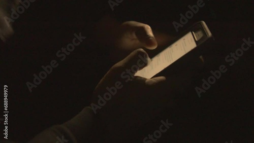 close up of a black mans hands scrolling his phone in the dark photo