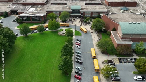 Students at public school campus buildings as school buses arrive to transport learners. Diversity DEI theme in American education. Aerial. photo