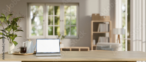 A white-screen laptop computer mockup on a wooden tabletop in a minimal Scandinavian living room.