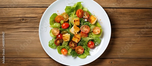 Top down view of mixed lettuce, cherry tomatoes, croutons and capelin roe on a white dish, resting on an aged wooden table.