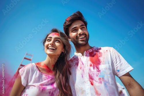 Loving couple of Indian ethnicity celebrating Holi festival with colours in a blue sky background 