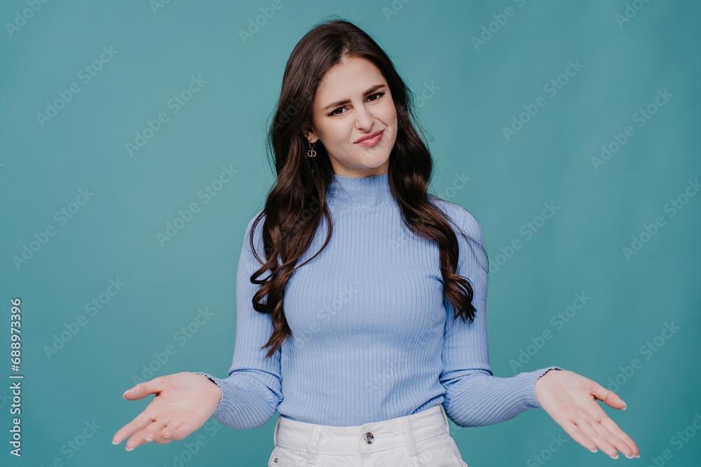 Unhappy brunette girl in casual sprees hands in disbelief expression looks at camera against turquoise studio background with copy space. Finally make a choice, no more doubts. Unhappy brunette girl in casual sprees hands in disbelief expression looks at camera against turquoise studio background with copy space. Finally make a choice, no more doubts.