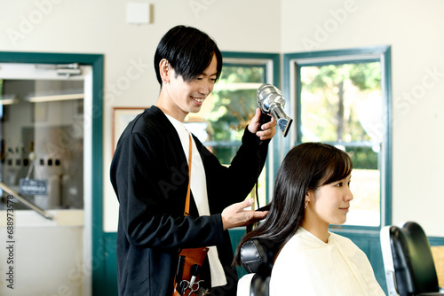 女性客の髪をドライヤーで乾かすアジア人の男性美容師