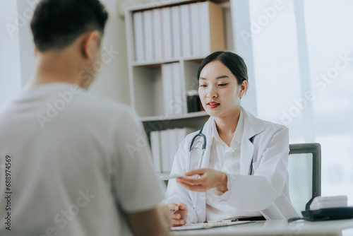 Asian female doctor discussing medicine bottle with male patient in hospital