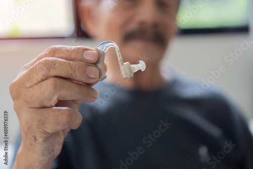 Senior man with grey hair holding medical hearing aid smiling happy and positive, doing showing a new one hearing aid. photo