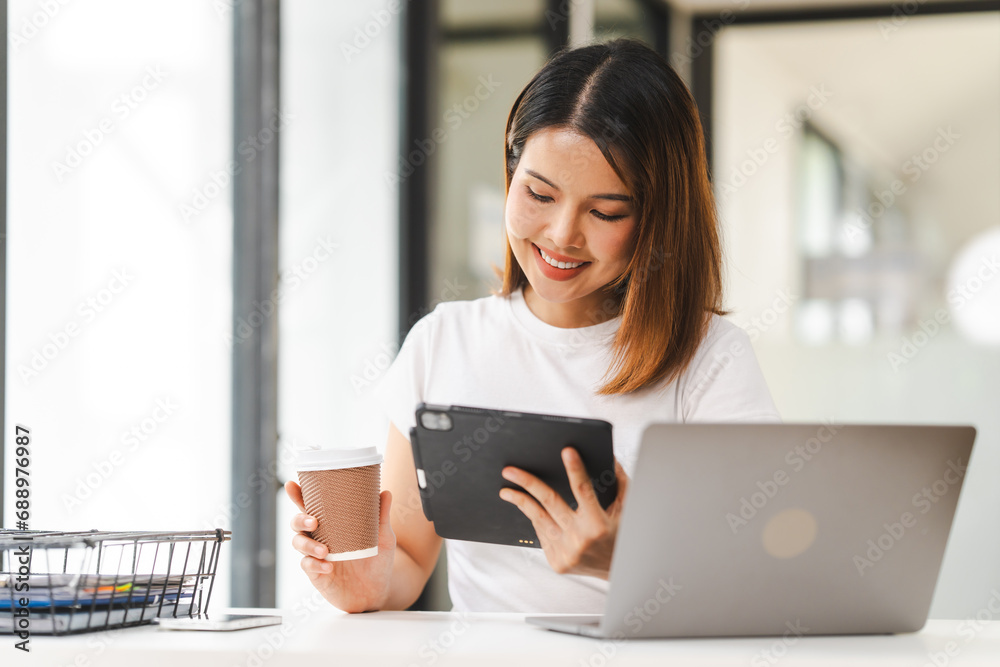 Cheerful Asian woman confidently uses mobile phone, tablet with laptop and notebooks on the desk in a bright office. Cheerful Asian woman confidently uses mobile phone, tablet with laptop and notebooks on the desk in a bright office.