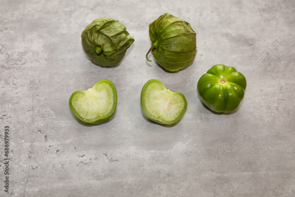 Mexican husk tomatoes also known as green tomatillos with the husk, whole without husk and cut in half. Mexican husk tomatoes also known as green tomatillos with the husk, whole without husk and cut in half.