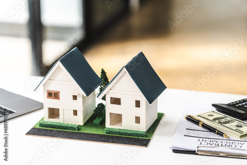 Two model houses on a desk with a laptop and paperwork, representing real estate property for sale or investment.