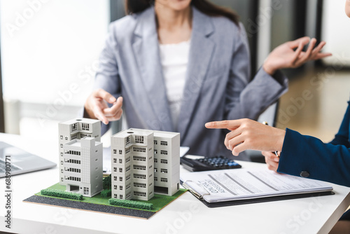 Two middle aged and young Asian business woman in formal suits discuss over model buildings, on city investment and development strategies. urban investment opportunities in city, condo, apartment.