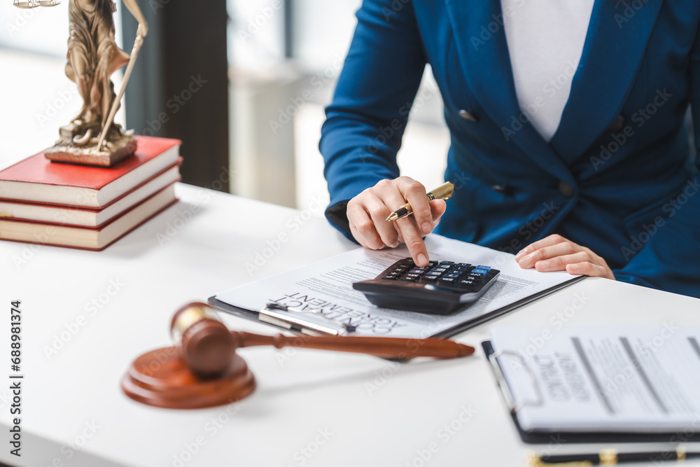 Close up of a lawyer calculating expenses, with a legal contract, gavel, and law books on the table. - obrazy, fototapety, plakaty 
