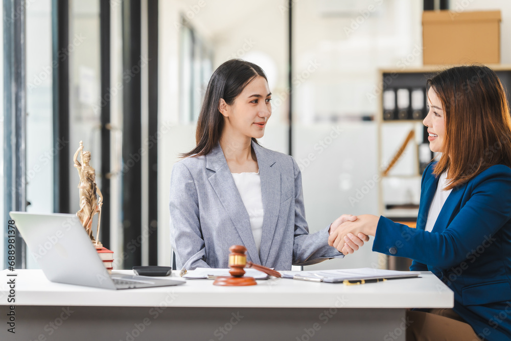 Two middle aged and young Asian lawyer in a formal suit consoles a client during a legal consultation, with a gavel and documents on the table. Two middle aged and young Asian lawyer in a formal suit consoles a client during a legal consultation, with a gavel and documents on the table.