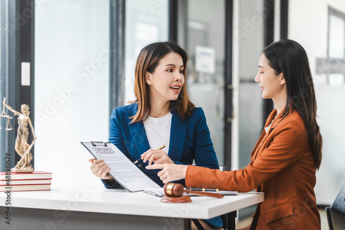 Two young and middle-aged Asian women lawyers in formal suits discuss legal contract, focusing on legislation and women's rights in law office.