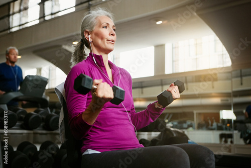 Senior fitness, dumbbell or old woman at gym for training, wellness or cardio with earphones, music or exercise. Weightlifting, bodybuilding and elderly female person at sports center for arm workout