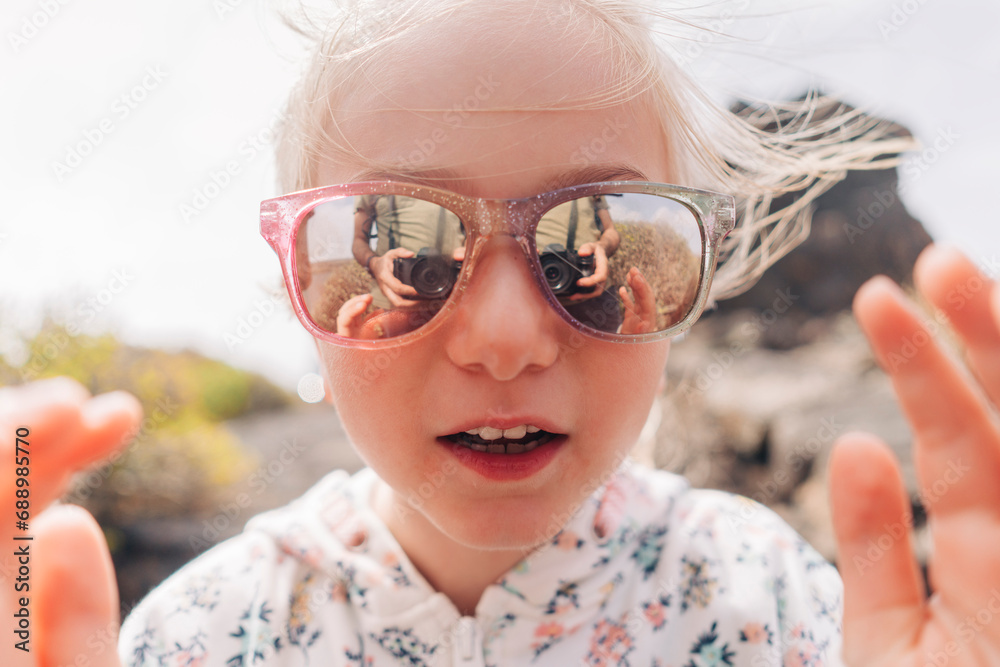 A child's curious eyes reflected in the lenses of a pair of pink sunglasses. A child's curious eyes reflected in the lenses of a pair of pink sunglasses.