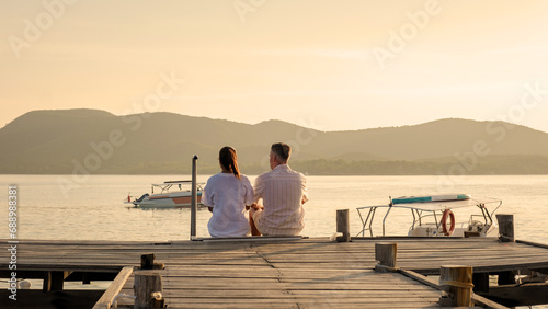 couple sitting on a wooden deck pier in the ocean during sunset in Samaesan Thailand photo