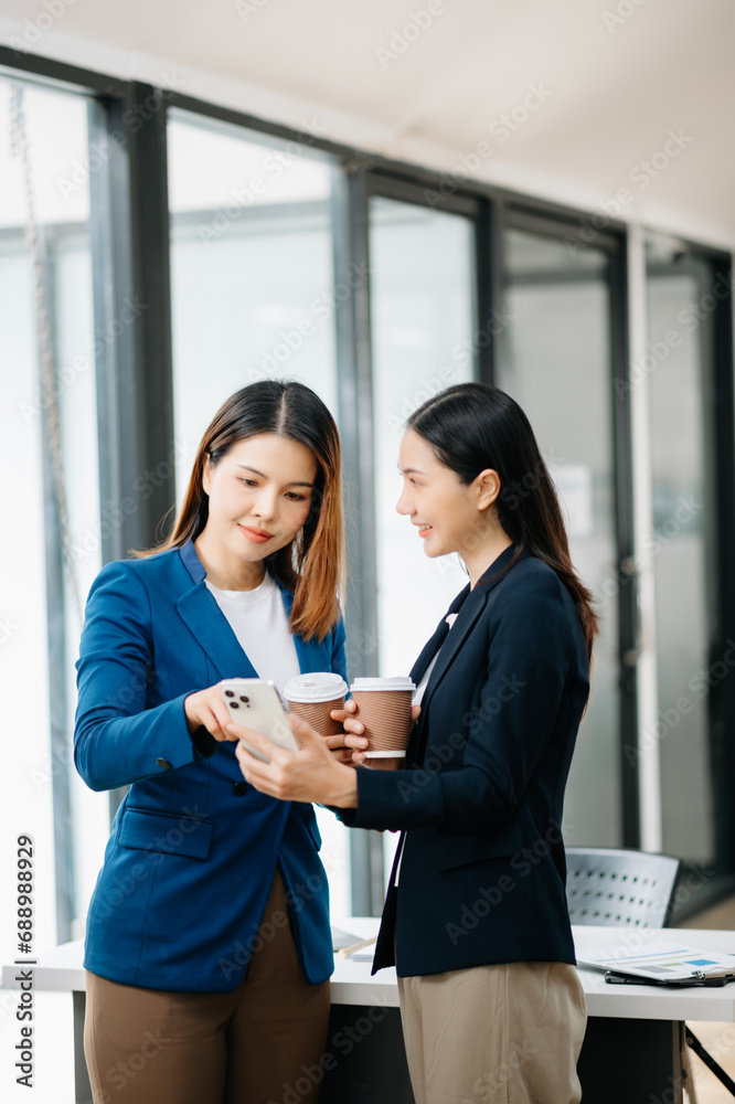 Obraz premium Happy two Asian business woman holding coffee cup in moderm office