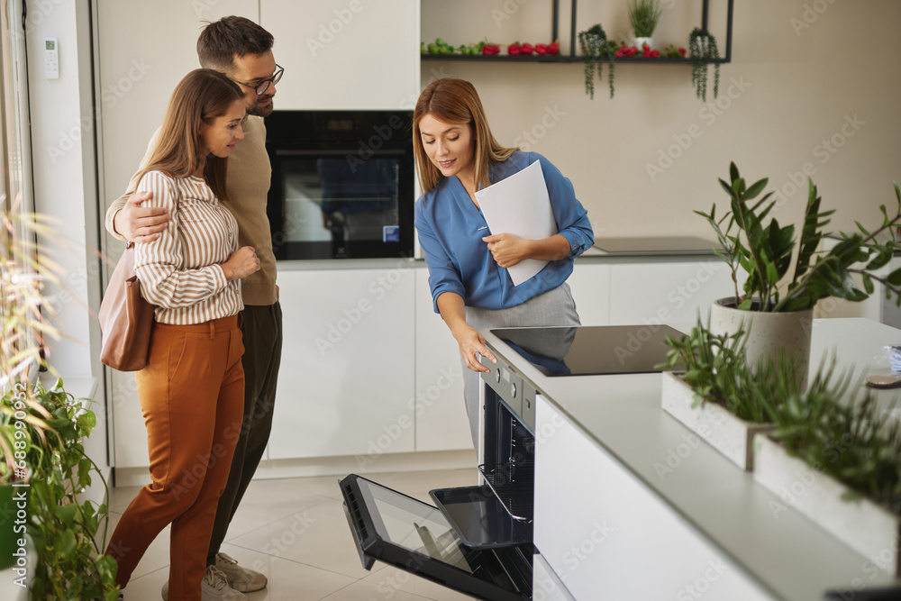 Female shop assistant helping young couple choose new electric stove Female shop assistant helping young couple choose new electric stove