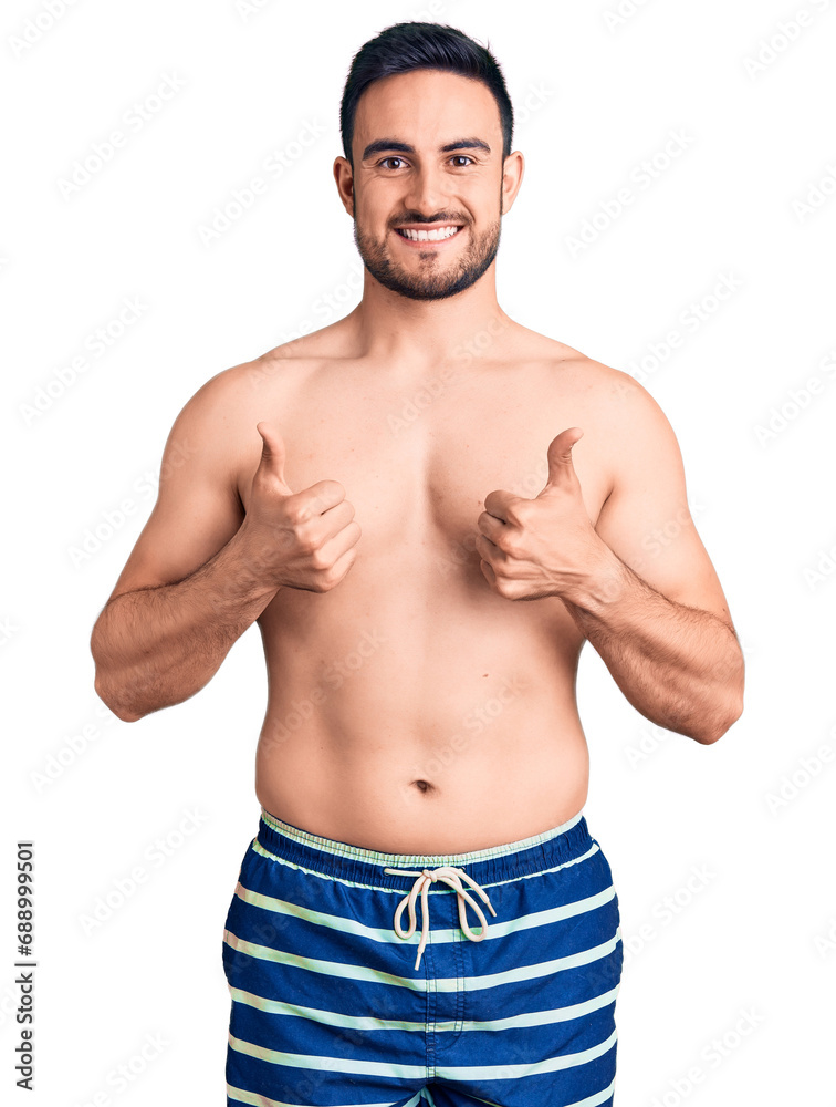 Young handsome man wearing swimwear success sign doing positive gesture with hand, thumbs up smiling and happy. cheerful expression and winner gesture.