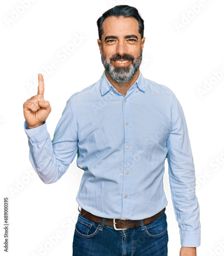 Middle aged man with beard wearing business shirt showing and pointing up with finger number one while smiling confident and happy.