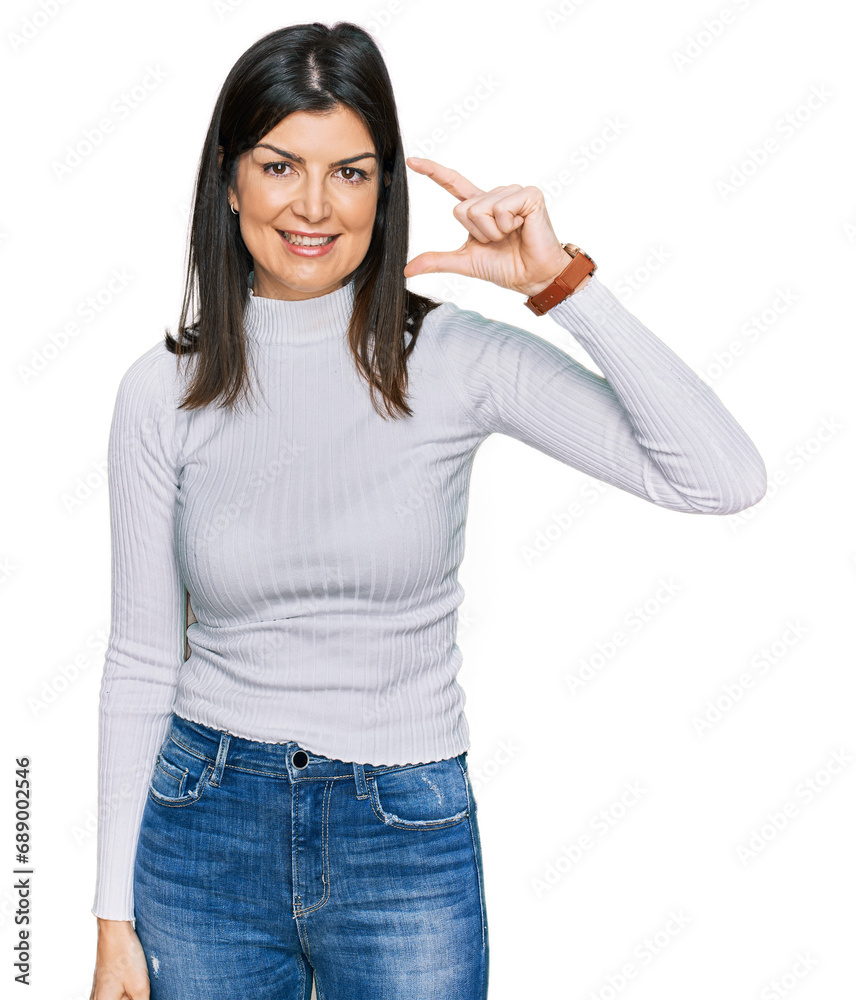 Beautiful brunette woman wearing casual clothes smiling and confident gesturing with hand doing small size sign with fingers looking and the camera. measure concept.