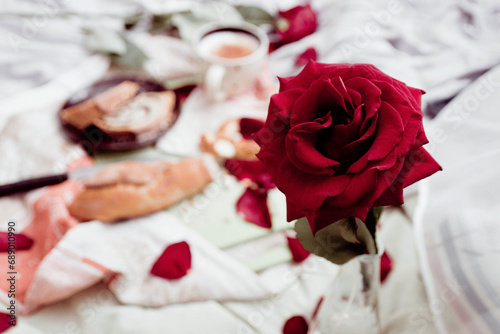 Breakfast in bed close-up, red rose and blanket, cappuccino in a light cup and pastries with poppy seeds on a board